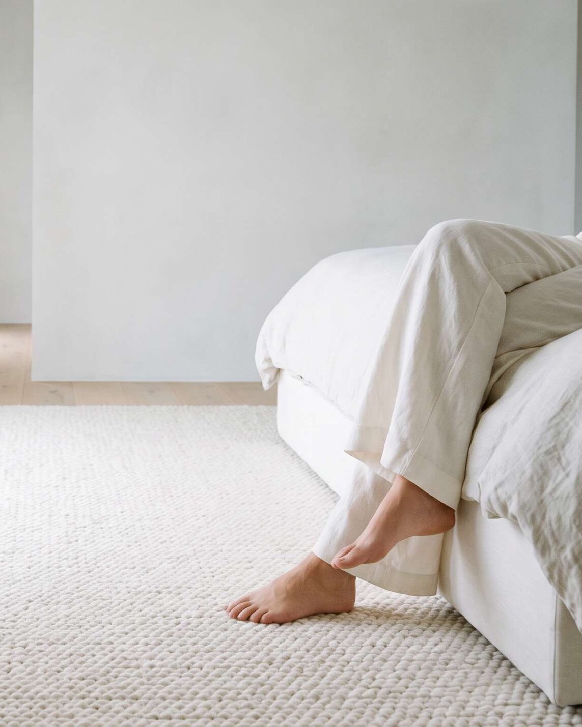 Bare feet stepping onto a soft cream wool rug beside the bed