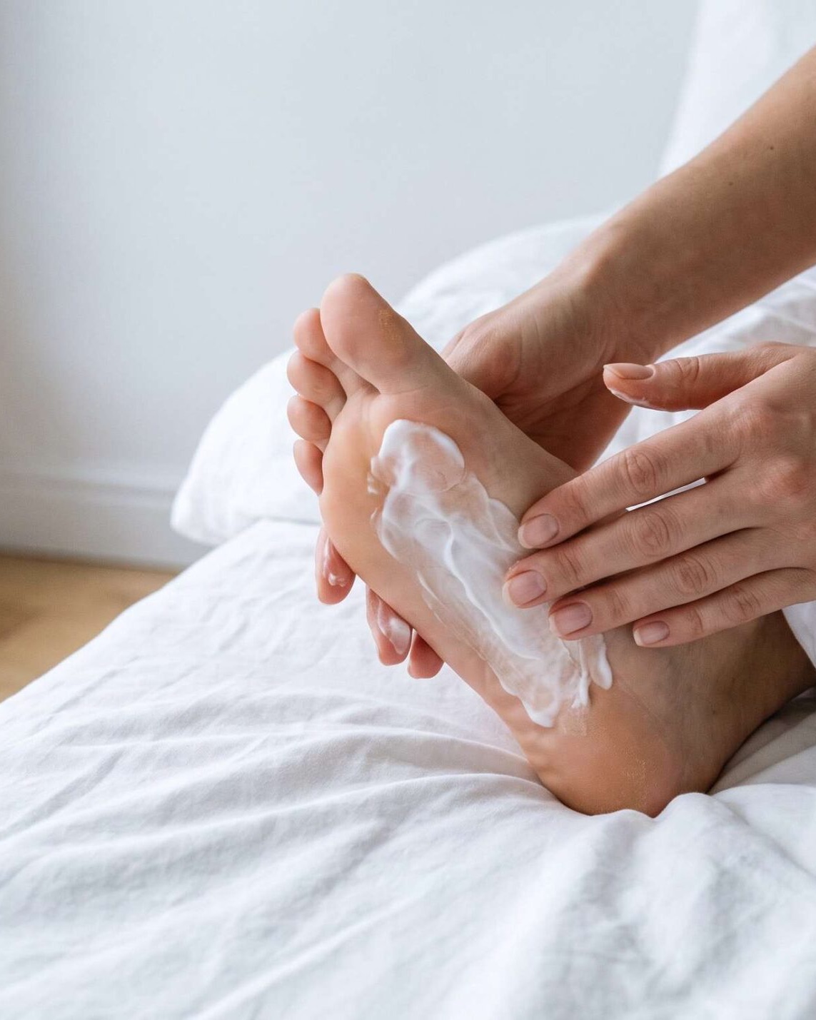 Close-up of hands massaging cream into a heel, bright white bedroom
