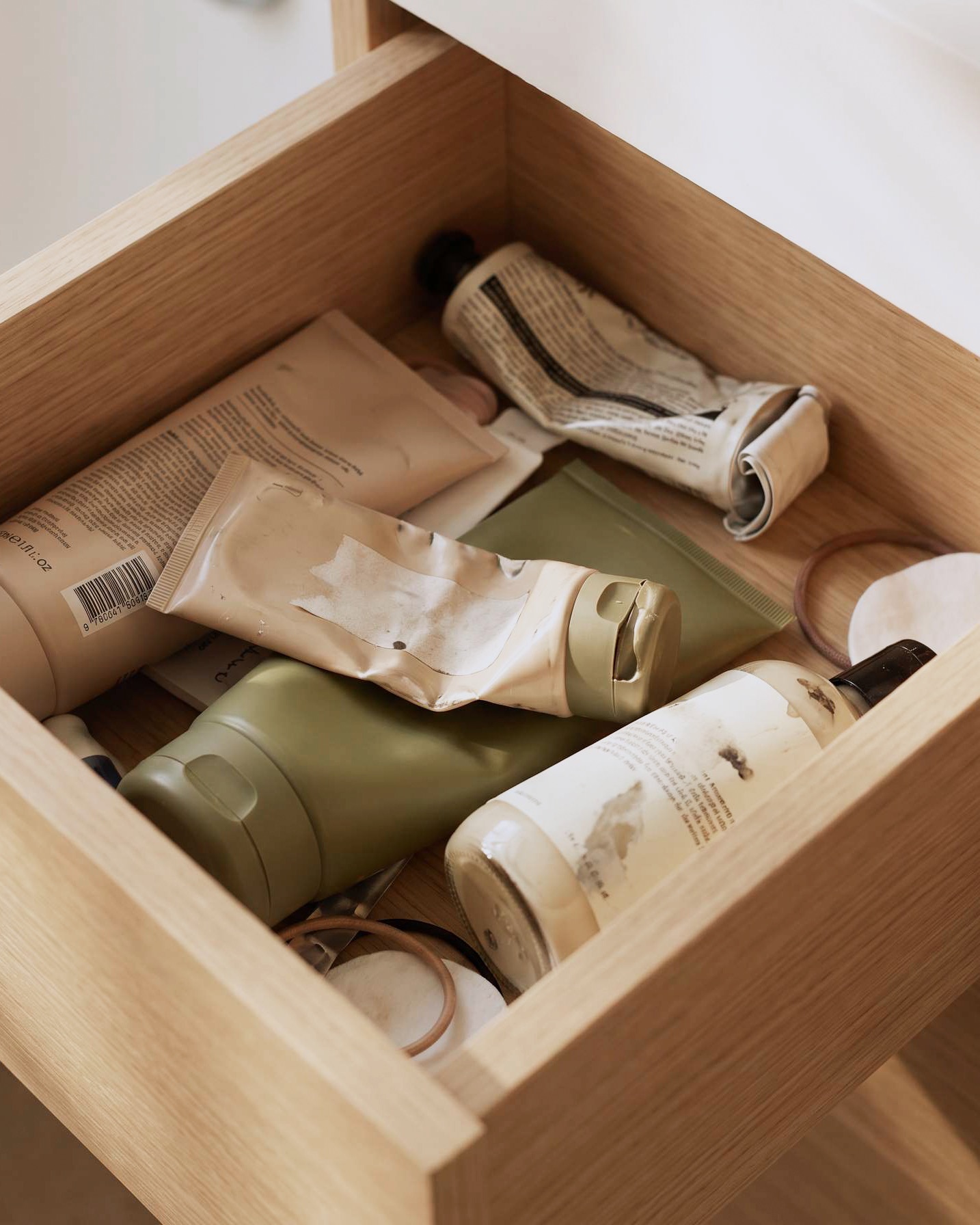 A half-open bathroom drawer crowded with half-used cream tubes and bottles